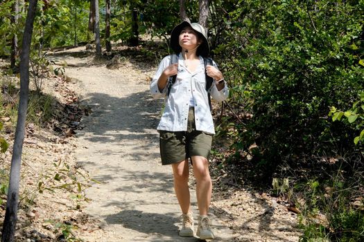 Happy Asian woman in a hat with a backpack trekking enjoying nature in the tropical forest. Travel and Lifestyle Concepts