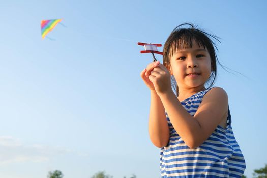 Child playing with a kite while running on a meadow by the lake at sunset. Healthy summer activity for children. Funny time with family.