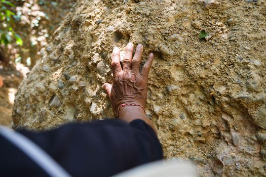 Elderly Asian male geologist researcher touches rocks with his hands to analyze surfaces in Mae Wang Natural Park, Thailand. Exploration Geologist in the Field