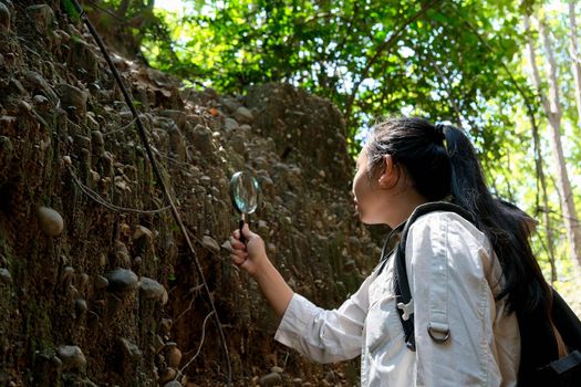 Asian female geologist researcher analyzing rocks with a magnifying glass in Mae Wang Nature Park, Thailand. Exploration Geologist in the Field