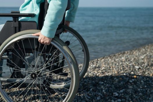 Caucasian woman in a wheelchair on the seashore. Close-up of female hands