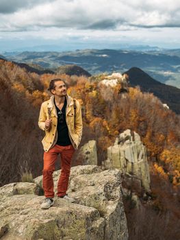 Traveler is standing on high rock, enjoying the view and looking up. Travel and hiking concept in autumn time