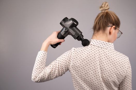 Caucasian business lady makes herself a back massage with a massager gun on a white background