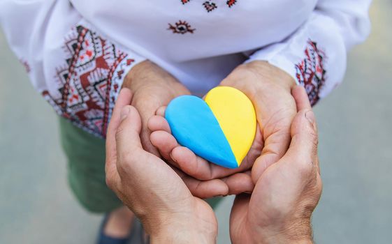Grandmother holds in her hands a heart in the color of the Ukrainian flag. Selective focus. People.