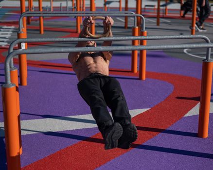 Shirtless man doing horizontal balance on parallel bars at sports ground