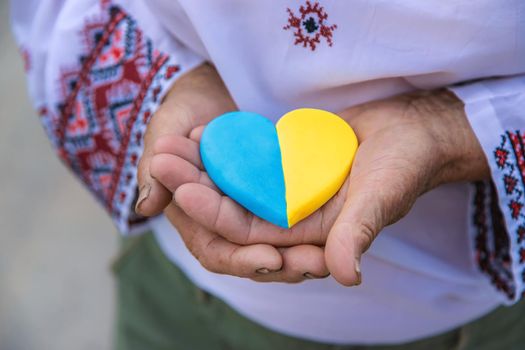 Grandmother holds in her hands a heart in the color of the Ukrainian flag. Selective focus. People.