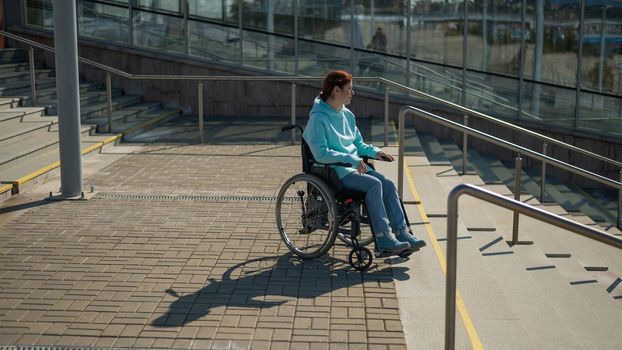 A caucasian woman in a wheelchair cannot go down stairs without a ramp. Hard to access environment