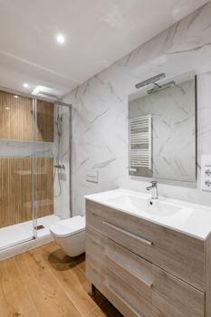 Simple and modern bathroom with marble white tiles, wooden finishing, toilet and shower.