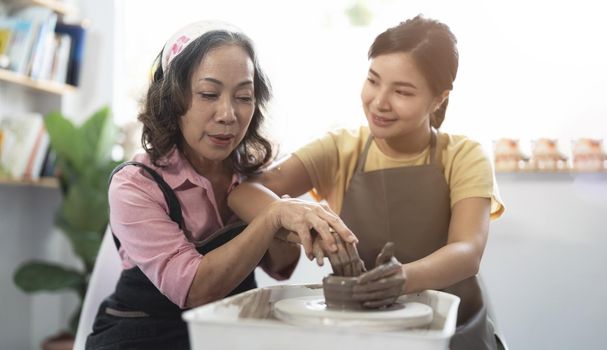 Pottery workshop. Senior teaches young asian woman pottery. Clay modeling.
