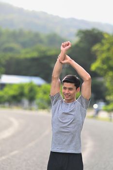 Handsome young man in sportswear warming up before sports training outdoors. Healthy lifestyle, workout and wellness concept.