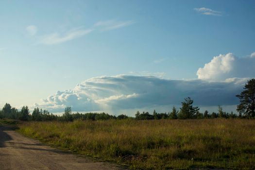 Landscape with dramatic sky and unripe wheat field at rainy summer season. Dirt road with dark storm clouds