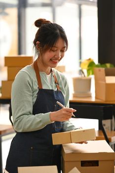 Smiling young woman prepare parcel boxes of product for shipping. E-Commerce, online business, online sales concept.