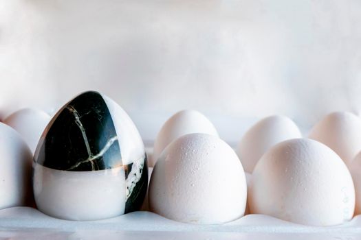 Eggs of different colors in cardboard boxes. A marble stone black-and-white egg stands in a cassette in the middle of white chicken eggs. The concept of contrast, individuality, exclusivity. concept of a damaged tooth