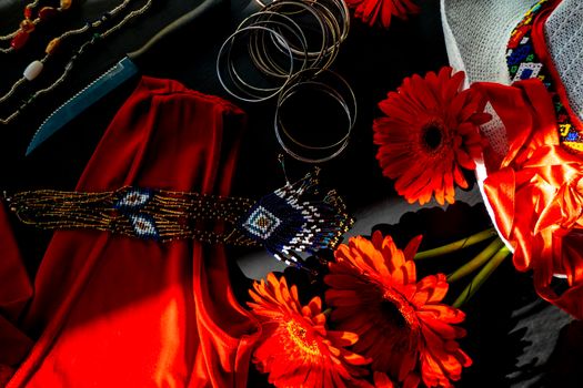 flat lay of a fashionable look from red and white accessories on a black background. Scarlet dress and white hat with a ribbon, jewelry made of beads and small stones, light jingling bracelets and a knife - as a symbol of passion and danger