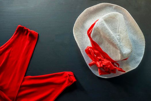 flat lay of a fashionable look from red and white accessories on a black background. Scarlet dress and white hat with ribbon