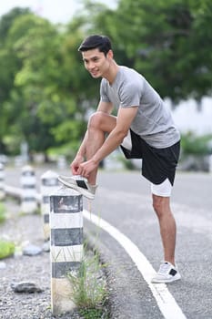 Handsome sportsman tying shoelaces before running, getting ready for jogging outdoors. Healthy lifestyle, workout and wellness concept.