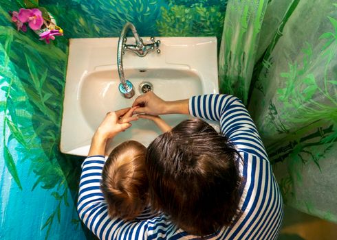 Son and father in vests wash their hands in a painted bathroom. the concept of hygiene. hands close up