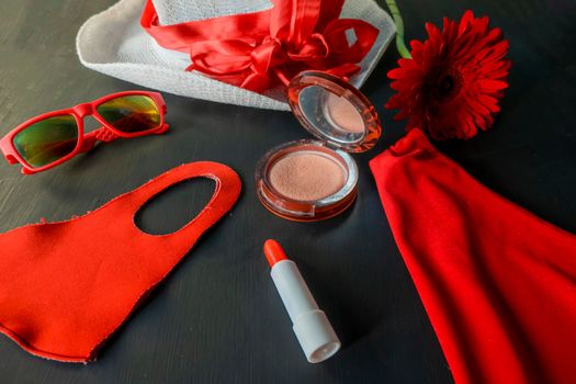 flat lay of a fashionable look from red and white accessories on a black background. A scarlet dress and a white hat with a ribbon, red lipstick, a fashionable medical mask, funny sunglasses.