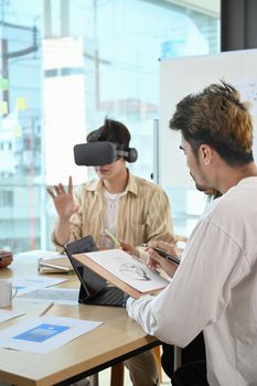Website development team testing virtual reality headset, brainstorming on augmented reality improvement, future technology for business.