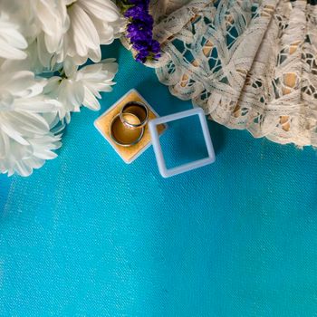 Wedding bouquet of bride. wedding card with original rings in a white box, a bouquet of white chrysanthemums or daisies and a white lace fan on a blue background