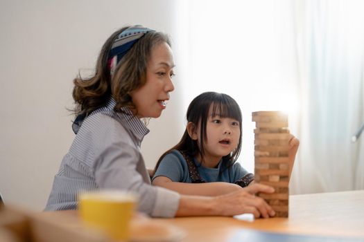 Happy moments of Asian grandmother with her granddaughter playing jenga constructor. Leisure activities for children at home.