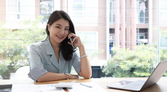 Beautiful young Asian businesswoman charming smiling and talking on the mobile phone in the office..