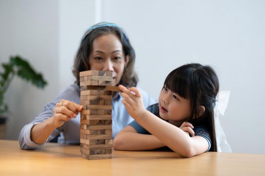 Little girl with her grandma playing jenga game at home.