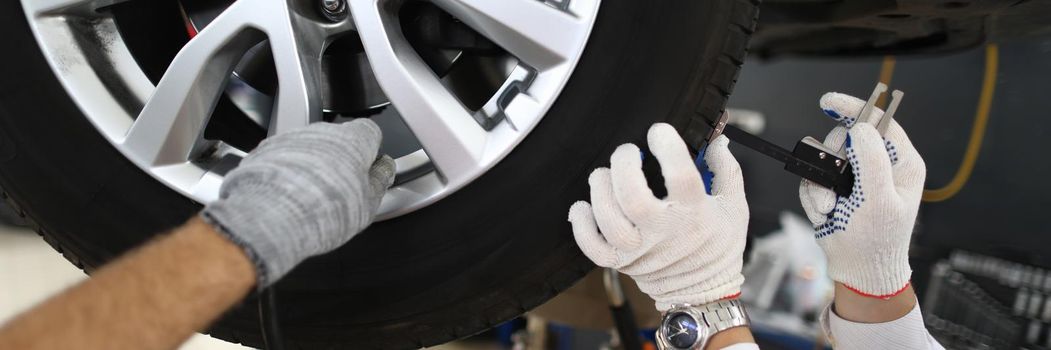 Men repairmen fixing car on lift in workshop closeup. Car repair and maintenance concept