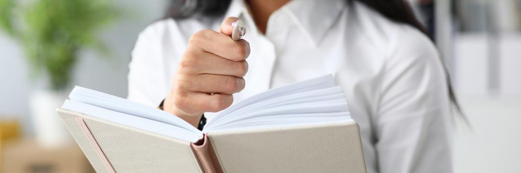 Young businesswoman holding notepad and ballpoint pen in office closeup. Organization and planning concept