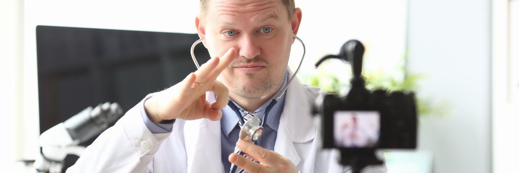 Male doctor banging on stethoscope in front of camera in clinic. Online medical training concept