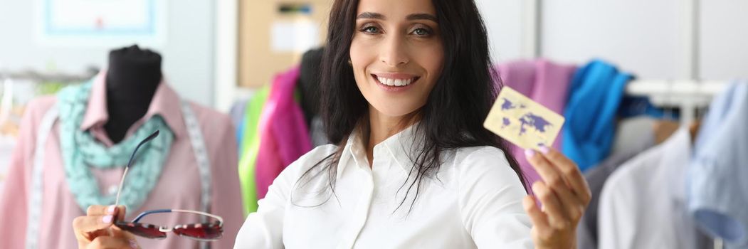 Smiling woman holding plastic credit card in clothing salon. Shopping and fashion concept