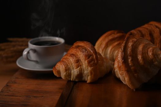 Tasty croissants and hot coffee on wooden wooden board ready to serve for breakfast. Breakfast, bread bakery products cafe concept.