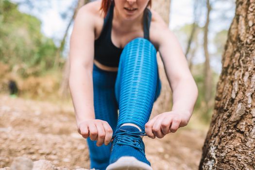 detail of the hands of a young girl athlete tying her trainers outside in a public park. sportswoman doing training exercises. health and wellness lifestyle. outdoor public park, natural sunlight.