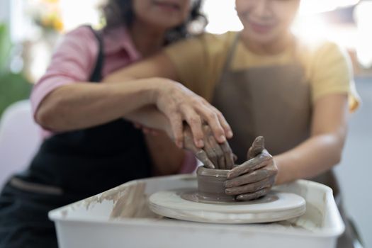Pottery workshop. Senior teaches young asian woman pottery. Clay modeling.