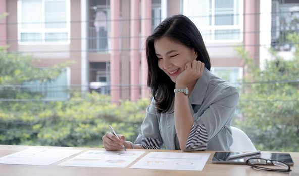 Beautiful Asian businesswoman analyzes charts using laptop calculator at the office..