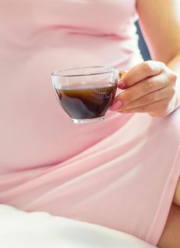 A pregnant woman is drinking coffee. Selective focus. people.