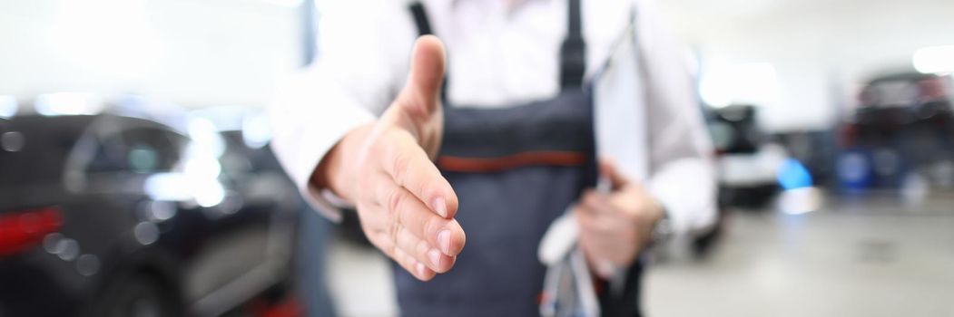 Male repairman stretching out his hand for handshake in car repair shop closeup. High quality car service concept