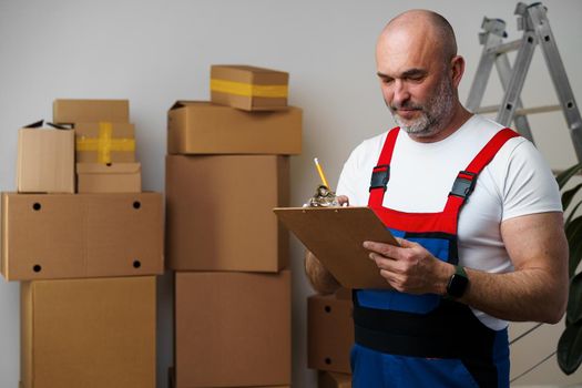 Middle-aged man mover in uniform making notes on clipboard, close up