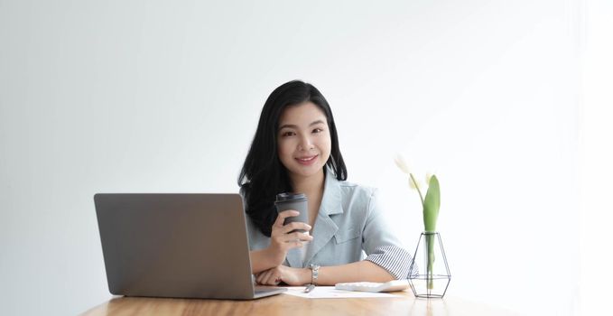 Smiling Asian businesswoman holding a coffee mug and laptop at the office. Looking at the camera..