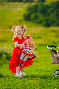 girl in a red dress and with a doll in her hands stands in nature