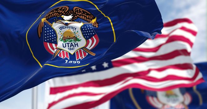 The Utah state flag waving along with the national flag of the United States of America. Utah is a state in the Mountain West subregion of the Western United States