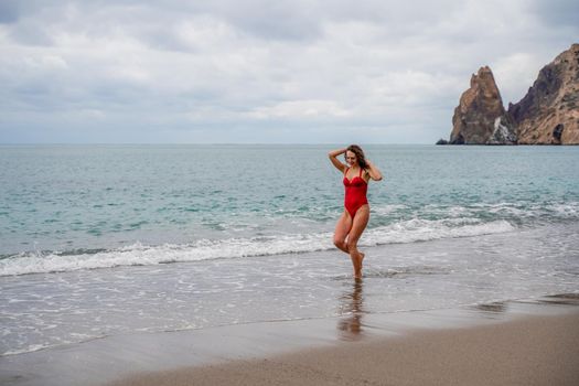 A beautiful and sexy brunette in a red swimsuit on a pebble beach, Running along the shore in the foam of the waves.