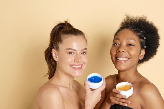 Two different women hold cosmetic patches under the eyes to remove dark circles under the eyes. Caucasian and African American female models take care of their skin, undergo anti-aging treatments, enjoy spa.