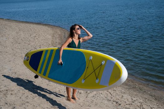 Caucasian woman walks along the beach and carries a sup board on the river in the city. Summer sport