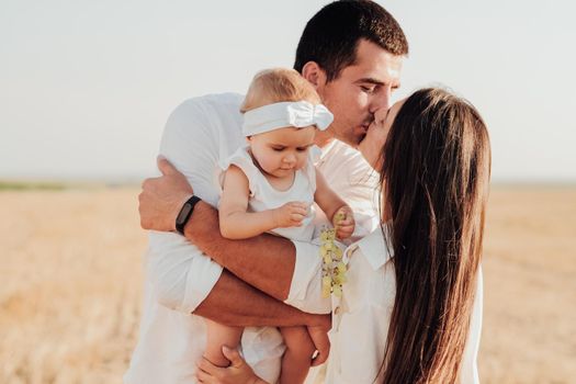 Young Caucasian Family with Toddler Child Hugging Outdoors in Field, Mother and Father Kissing While Their Daughter Eating Grape