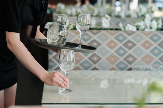 Female Waiter Serving Table with Water Glass for Guest in Restaurant