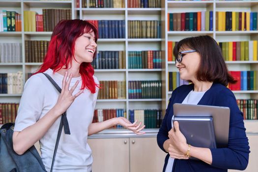 Female teacher talking to teenage student girl, inside library. Education, knowledge, studies, high school, college, young people concept