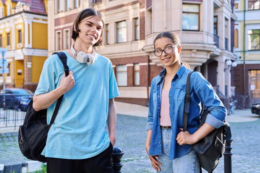 Portrait of teenage young guy and girl students looking at camera, outdoor. Couple of young people with backpacks, on city street. Teenagers, lifestyle, urban style, joy, friendship, education concept