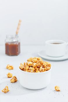 Sweet caramel popcorn in a ceramic bowl on a gray background with a jar of caramel and tea. Vertnical photo