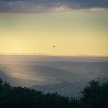 Evening view near to sunset from the top of Butser Hill, the highest point on the chalk ridge of the South Downs, over fields below with a hot air balloon on the horizon, Hampshire, UK